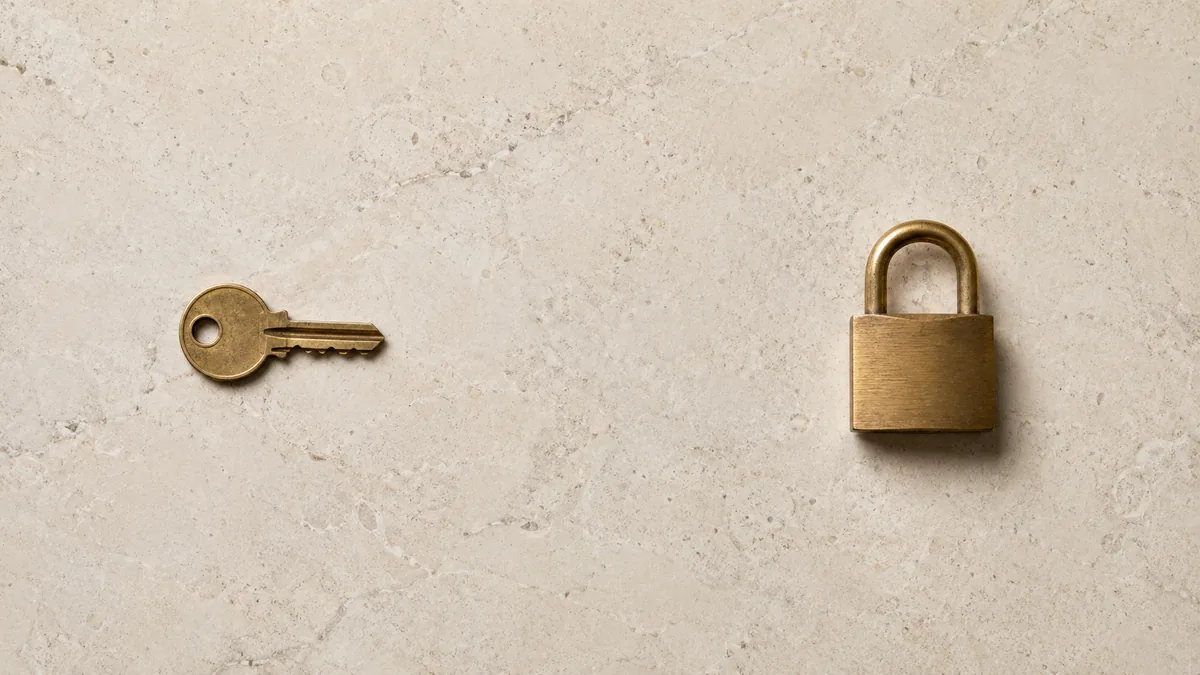 A brass key and a brass padlock separated on limestone